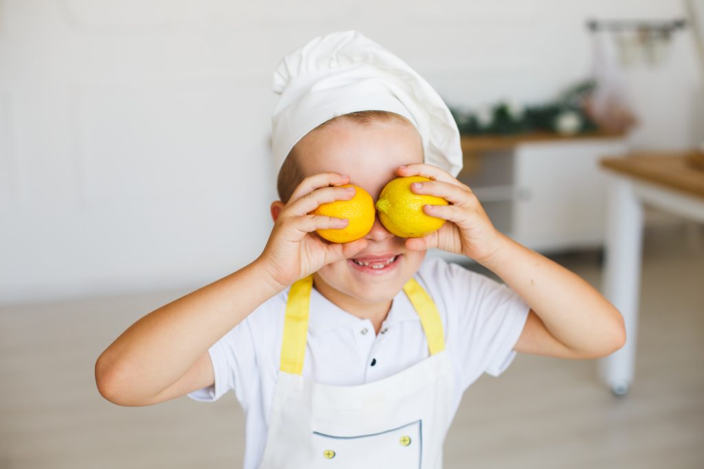 child in white polo shirt holding yellow fruit