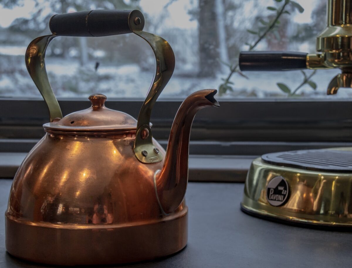 copper kettle and brass espresso machine near glass window